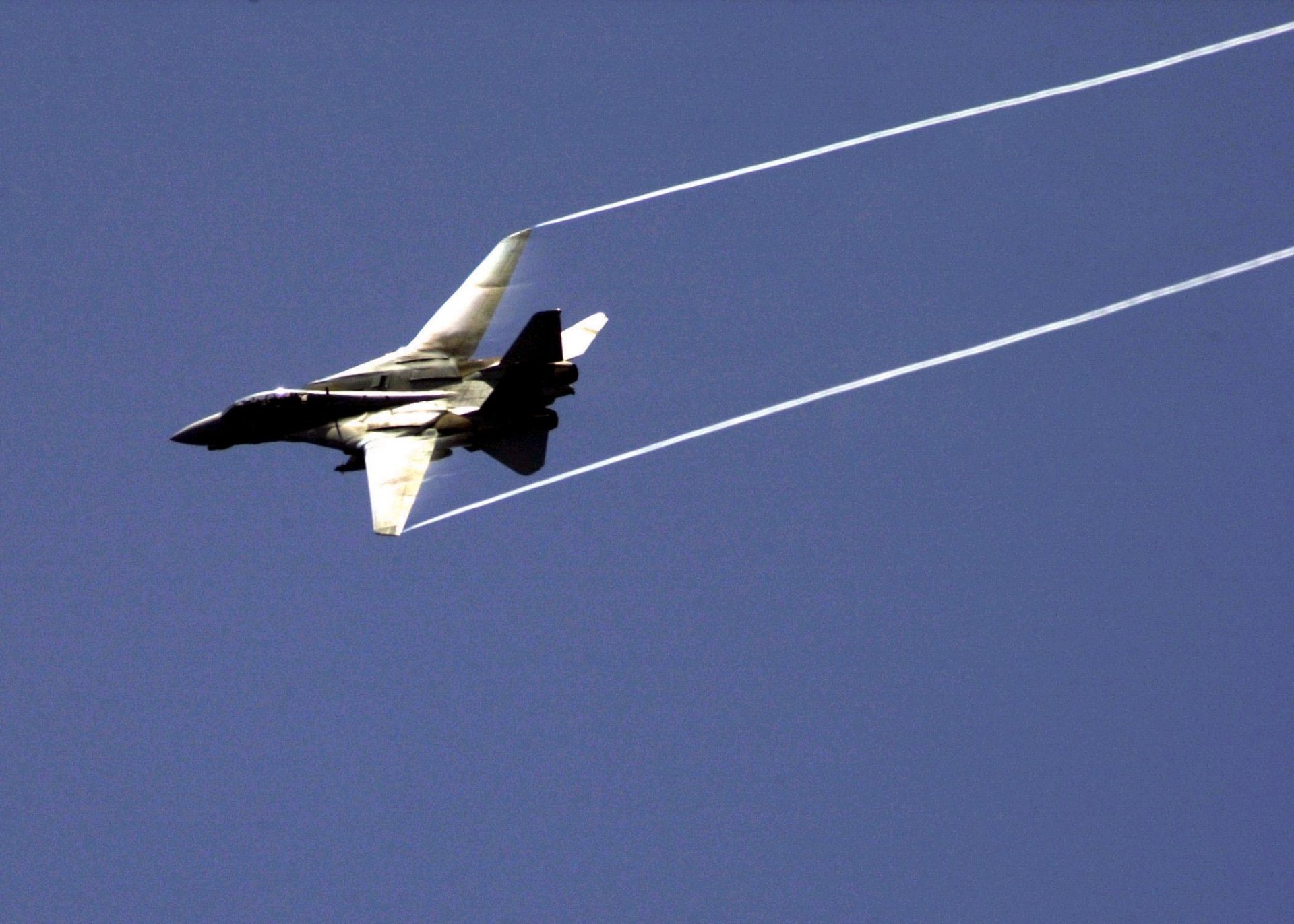 HD desktop wallpaper featuring a military Grumman F-14 Tomcat jet soaring against a clear blue sky, leaving white vapor trails.