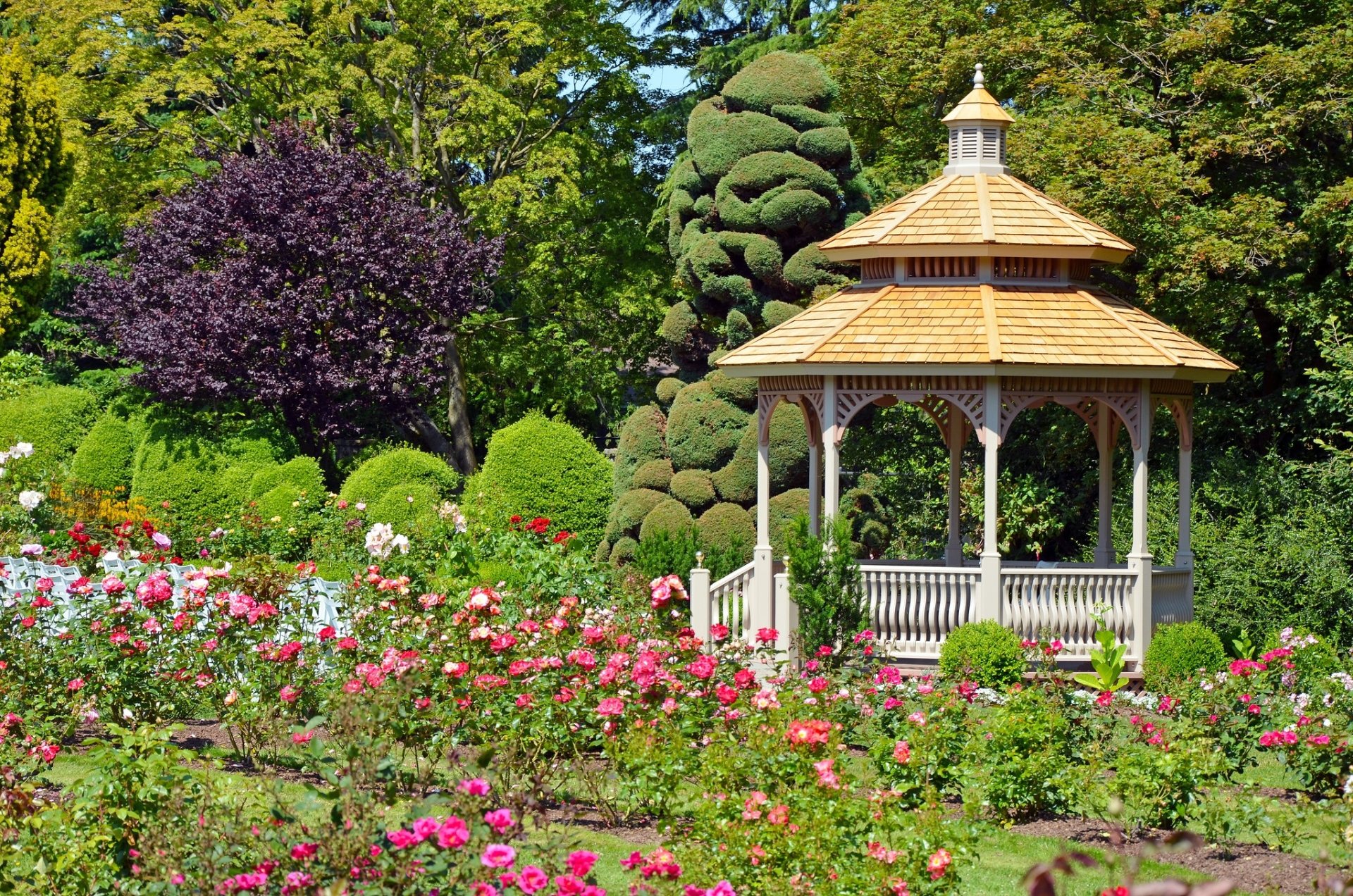 A vibrant park scene featuring blooming flowers surrounding a wooden gazebo, captured in HD quality for a serene desktop wallpaper background.