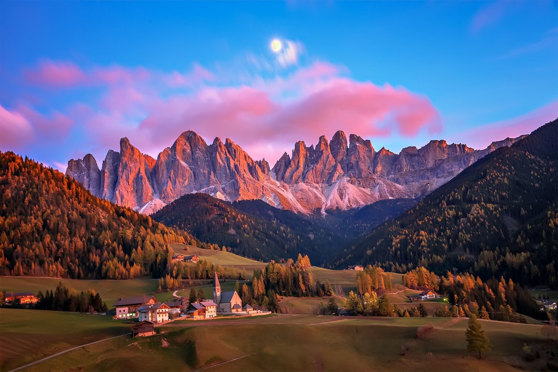 A vibrant HD wallpaper showcasing a charming man-made village set against the stunning Dolomites mountain range in Italy under a colorful sky.