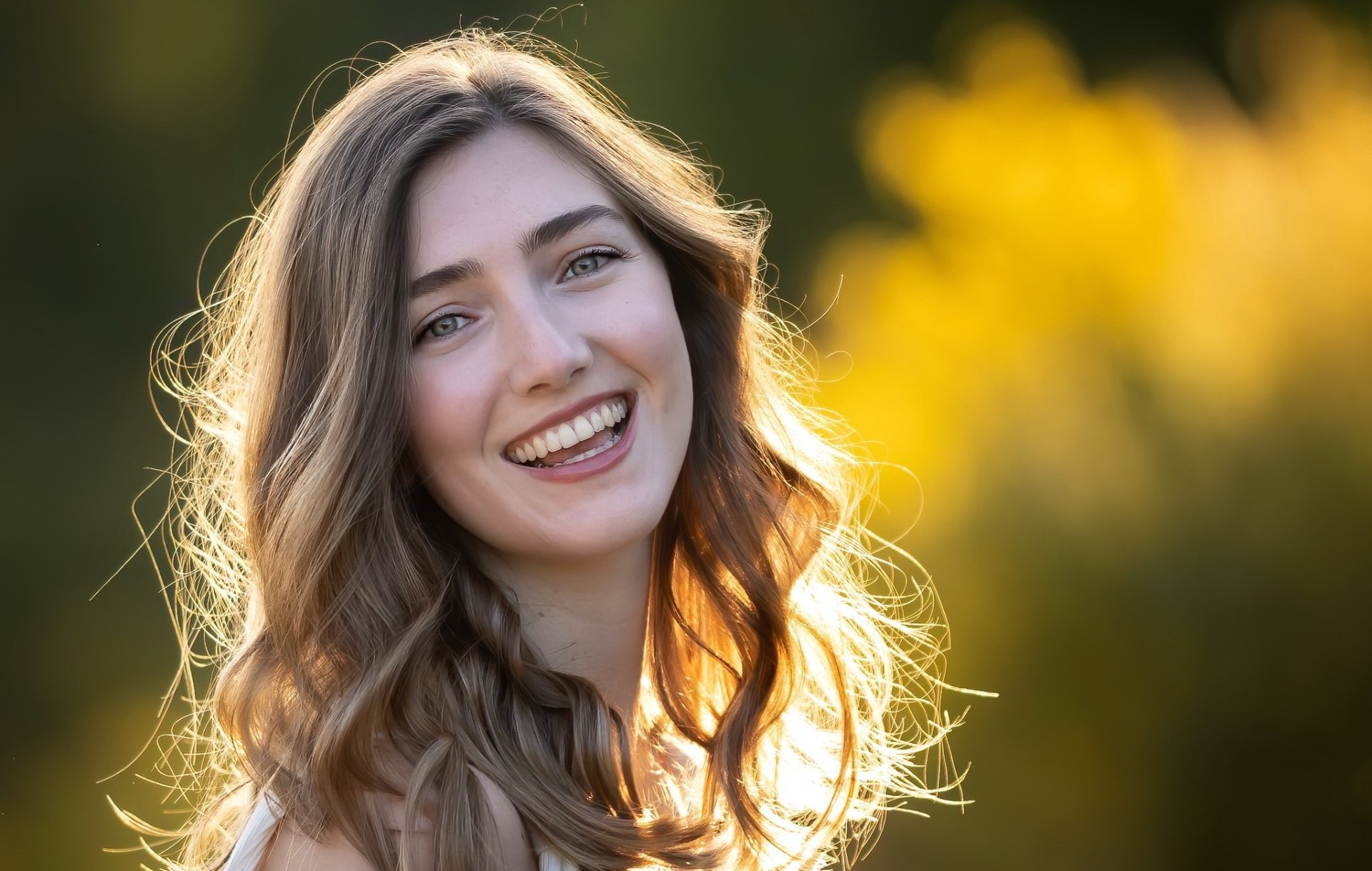 HD PC desktop wallpaper showing a smiling woman’s face with sunlit hair glowing against a soft golden bokeh background.