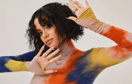 HD desktop wallpaper of a musician with wavy dark hair wearing a colorful tie-dye turtleneck, hands raised in a stylish, music-themed portrait.