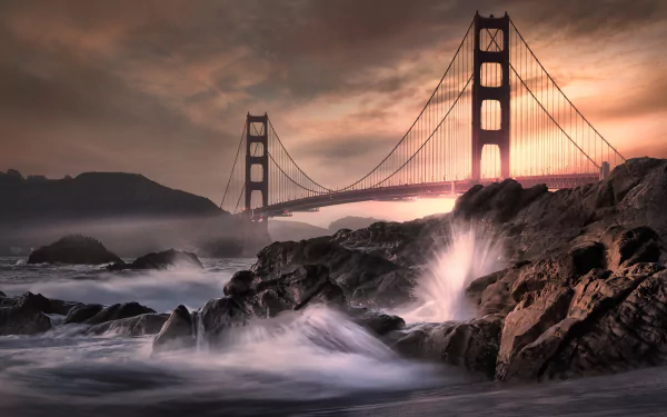4K Ultra HD wallpaper of the Golden Gate Bridge at sunset, showcasing man-made architecture against a dramatic sky and crashing ocean waves on rocky shores.