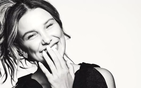 Black-and-white 2K desktop wallpaper: close-up of a smiling young woman, hand to mouth, relaxed studio portrait showing her face and joyful expression.