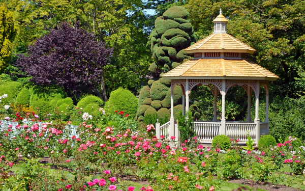 A vibrant park scene featuring blooming flowers surrounding a wooden gazebo, captured in HD quality for a serene desktop wallpaper background.