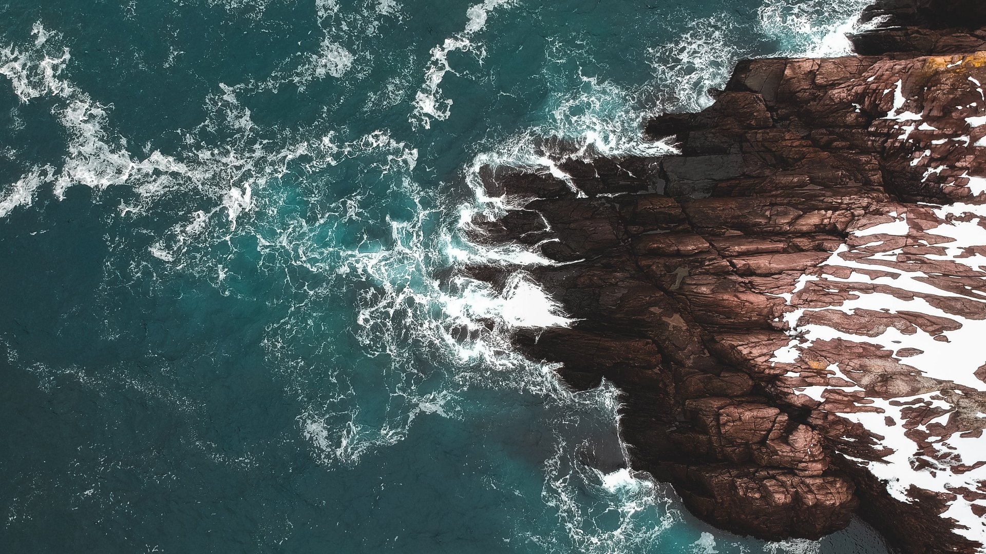 Aerial ocean photography: foam-laced turquoise waves crashing against a dark rocky coast — 4K Ultra HD PC desktop wallpaper and background.