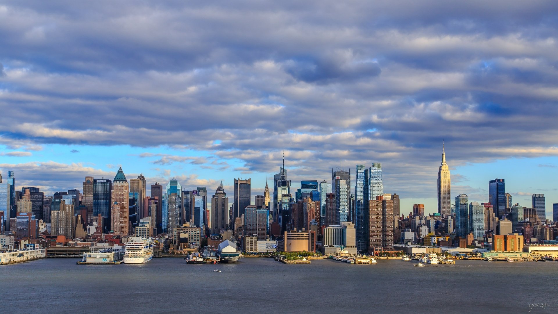 4K Ultra HD PC desktop wallpaper of New York's man-made skyline along the waterfront, cruise ships and towering skyscrapers beneath dramatic cloud-filled skies.