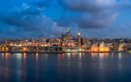 Valletta, Malta skyline at dusk: illuminated domes and historic buildings reflecting on calm harbor waters — 2K Quad HD PC desktop wallpaper of city architecture.