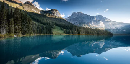 4K Ultra HD image of a serene lake in Alberta, Canada, reflecting majestic mountains and dense forest under a clear blue sky.