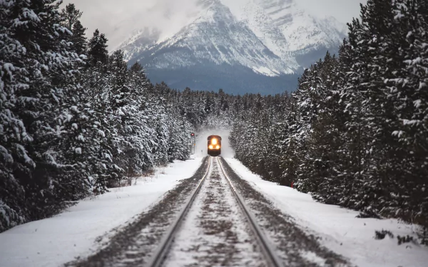 Train traveling through snowy tracks in a wintery forest, with a mountain in the background. This HD desktop wallpaper captures the serene beauty of a winter landscape.