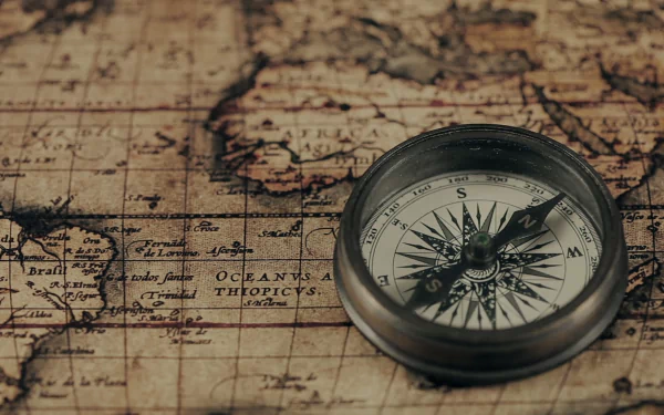 HD PC desktop wallpaper showing an antique map with man-made navigational markings and a metal compass resting on aged parchment.