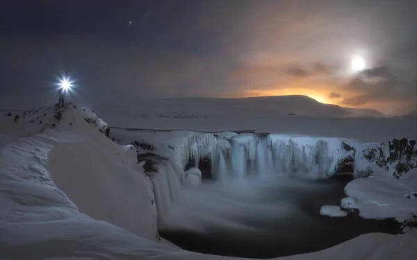 Iceland’s frozen Goðafoss waterfall at night, surrounded by snow and ice, illuminated subtly against a moody sky, captured in an HD desktop wallpaper.
