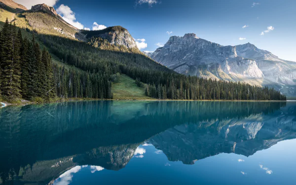 4K Ultra HD image of a serene lake in Alberta, Canada, reflecting majestic mountains and dense forest under a clear blue sky.