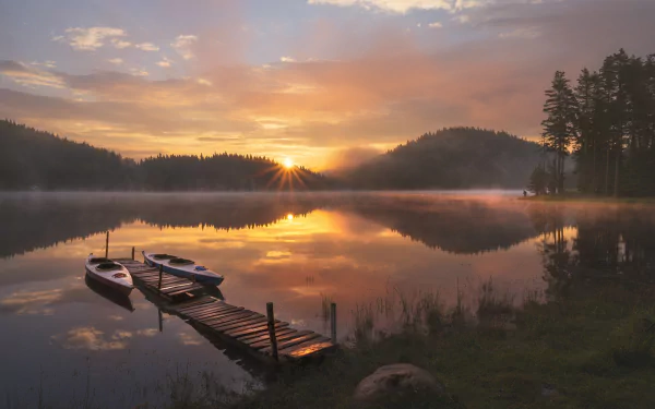 A kayak rests by a wooden dock on a calm river at sunset, with the sun casting golden reflections and silhouetted trees in the background. HD PC desktop wallpaper.