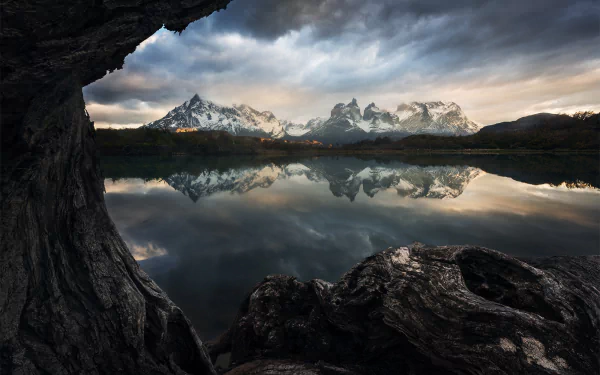 HD PC desktop wallpaper/background: snow-capped Andes mountains reflected in a calm lake, rocky foreground and dramatic cloudy sky.
