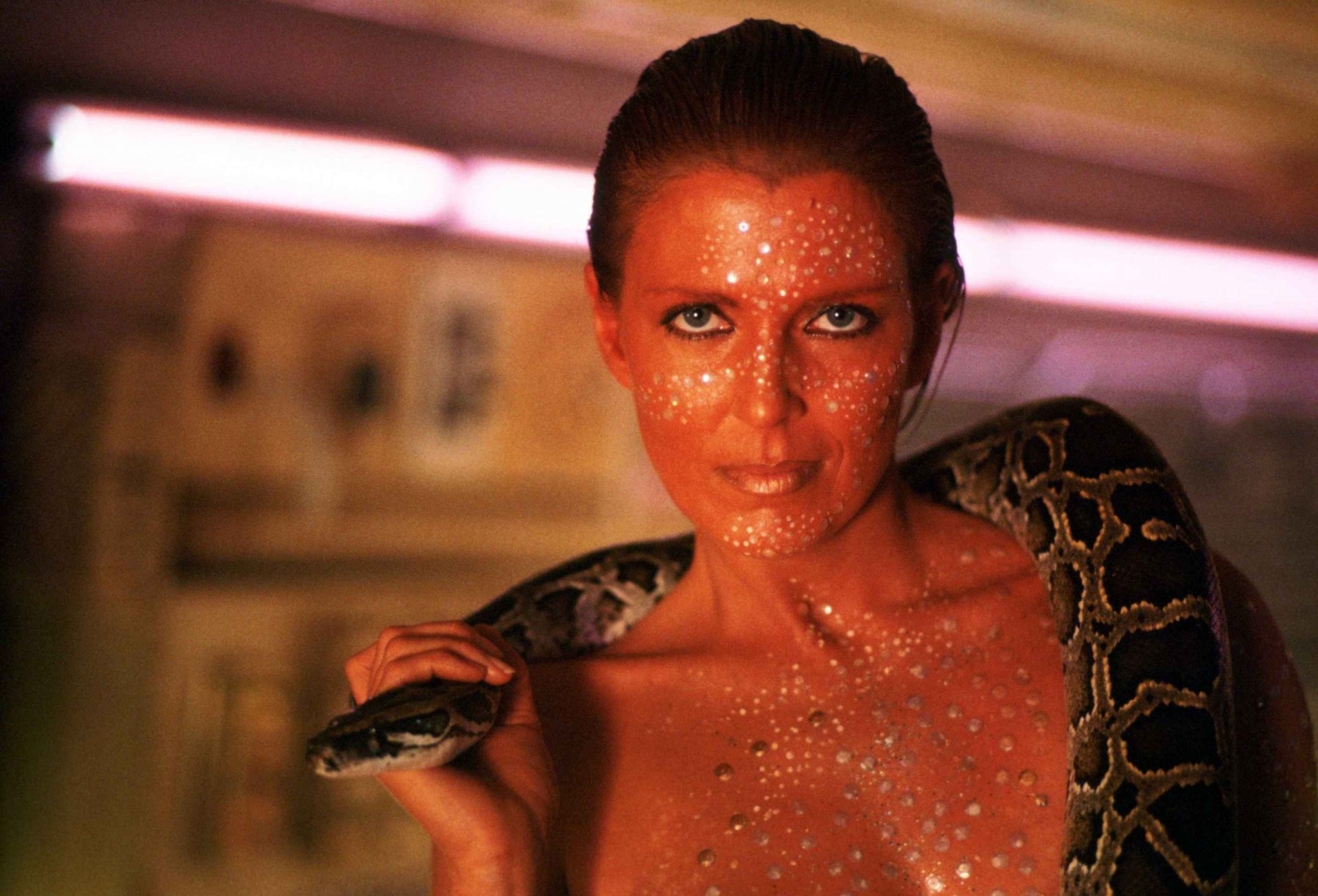 A striking HD desktop wallpaper from the movie Blade Runner, featuring a woman with sparkling skin holding a snake, set against a futuristic backdrop.