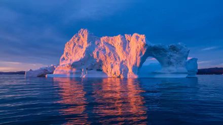 HD PC desktop wallpaper of an Arctic landscape featuring a sunlit iceberg with a natural arch rising from calm ocean waters under a clear blue sky.