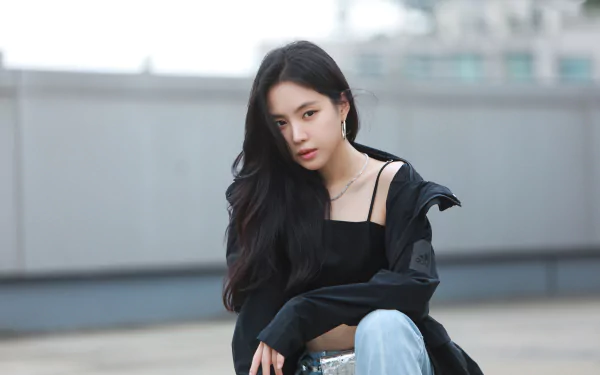 Female singer with long black hair seated on a rooftop in a casual jacket and crop top, moody urban 4K desktop wallpaper evoking music and style.