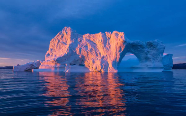 HD PC desktop wallpaper of an Arctic landscape featuring a sunlit iceberg with a natural arch rising from calm ocean waters under a clear blue sky.