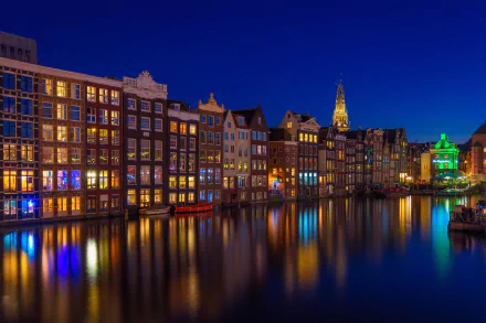 Night view of illuminated historic houses along a calm canal in Amsterdam, Netherlands, showcasing classic man-made architecture in an HD desktop wallpaper.