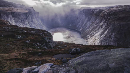 4K Ultra HD PC desktop wallpaper: dramatic mountain fjord framing a glassy lake below, rugged rock foreground and mist-filled valley under a moody sky.