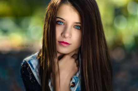 HD desktop wallpaper featuring a close-up portrait of brunette model Ariadna Velazquez with striking blue eyes and vibrant lipstick against a blurred natural background.