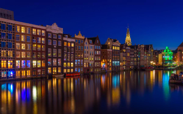 Night view of illuminated historic houses along a calm canal in Amsterdam, Netherlands, showcasing classic man-made architecture in an HD desktop wallpaper.