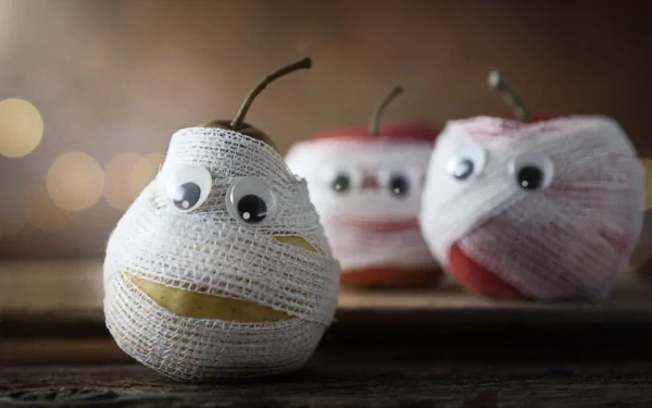 4K Ultra HD PC desktop wallpaper/background: funny food scene of a pear and two apples wrapped as mummies with googly eyes, staged on a rustic wooden tabletop.