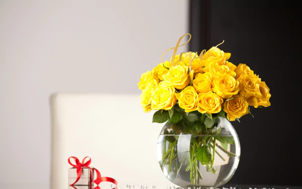 A vibrant bouquet of yellow roses arranged in a clear vase beside a small gift, captured in 4K Ultra HD as a PC desktop wallpaper and background.