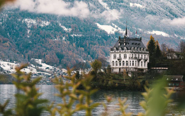 4K Ultra HD wallpaper of a grand mansion resembling a castle by a serene pond, set against a backdrop of misty mountains and autumnal foliage.