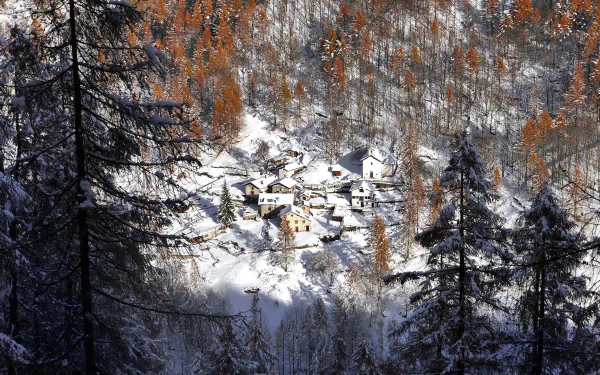 Snow-covered village nestled in a winter forest in Lombardy, Italy, surrounded by tall trees and autumn-colored foliage, captured in an HD desktop wallpaper.