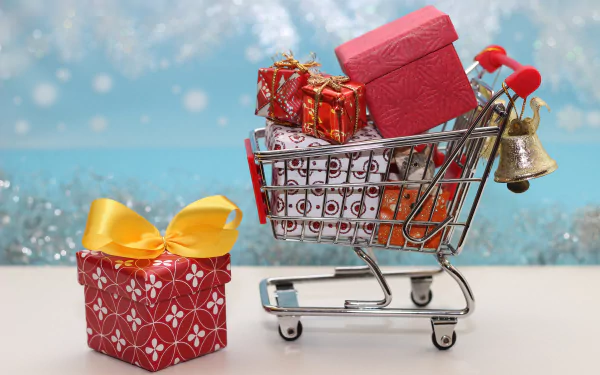 A festive 4K Ultra HD desktop wallpaper featuring a shopping cart filled with wrapped Christmas gifts and a bell, with a large gift box beside it against a snowy background.