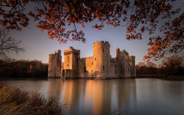 Bodiam Castle, a man-made medieval building in England, its stone walls reflected in a calm lake beneath autumn branches — HD desktop wallpaper.