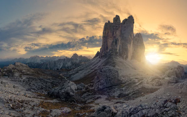 Tre Cime di Lavaredo in the Dolomites at dawn, golden sun breaking behind jagged peaks over a rocky foreground — 4K Ultra HD PC desktop wallpaper and nature background.