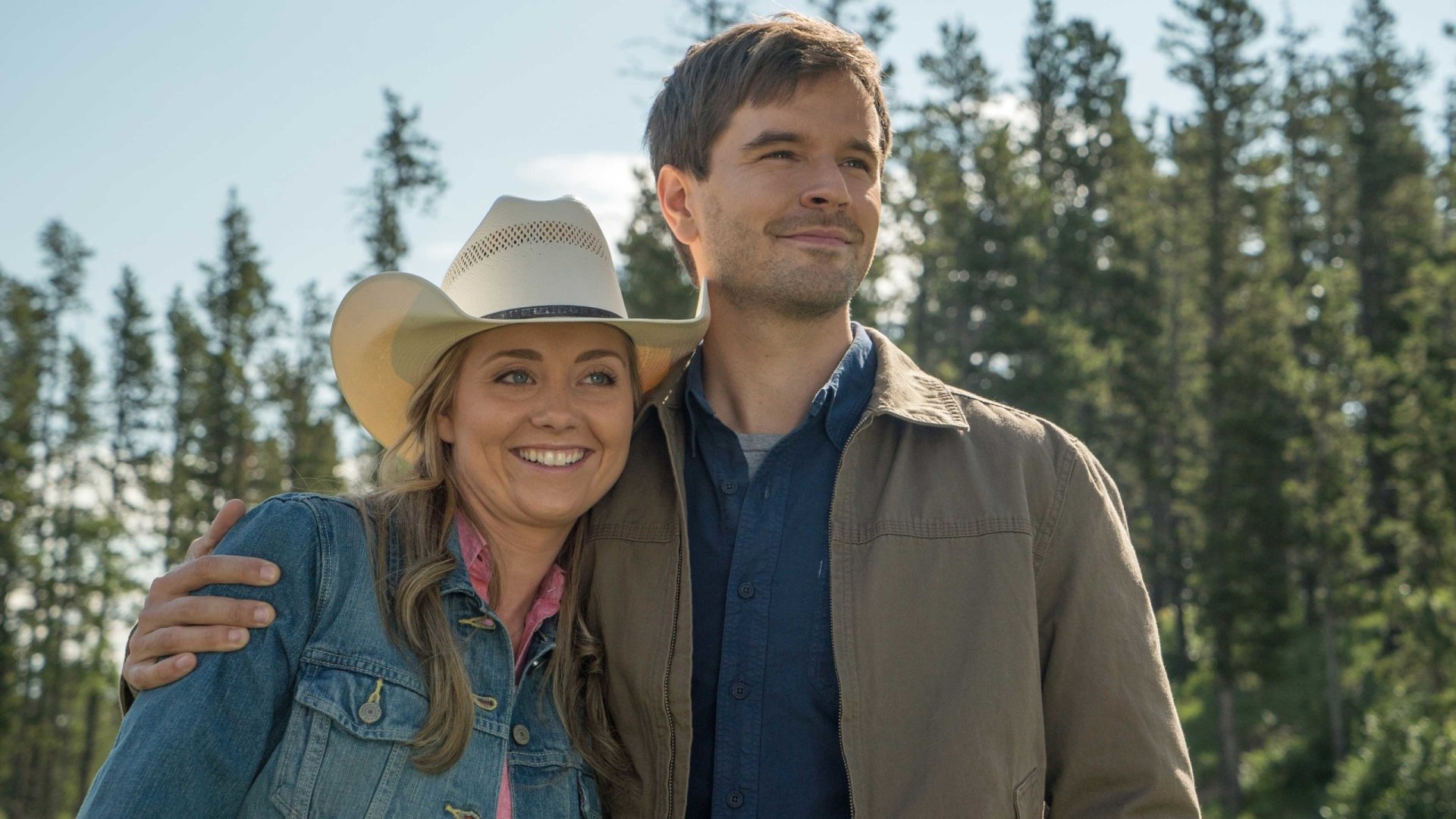 HD wallpaper of two smiling characters from the Heartland TV series, standing outdoors with trees in the background.