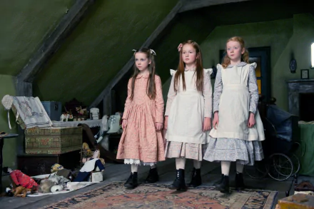 Three girls in Victorian dresses stand in a dim attic among scattered toys, eerie scene from the movie The Woman In Black — HD PC desktop wallpaper and background.