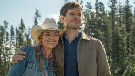 HD wallpaper of two smiling characters from the Heartland TV series, standing outdoors with trees in the background.