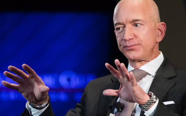 HD desktop wallpaper featuring a person with a bald head and suit, gesturing with hands, against a blue background.