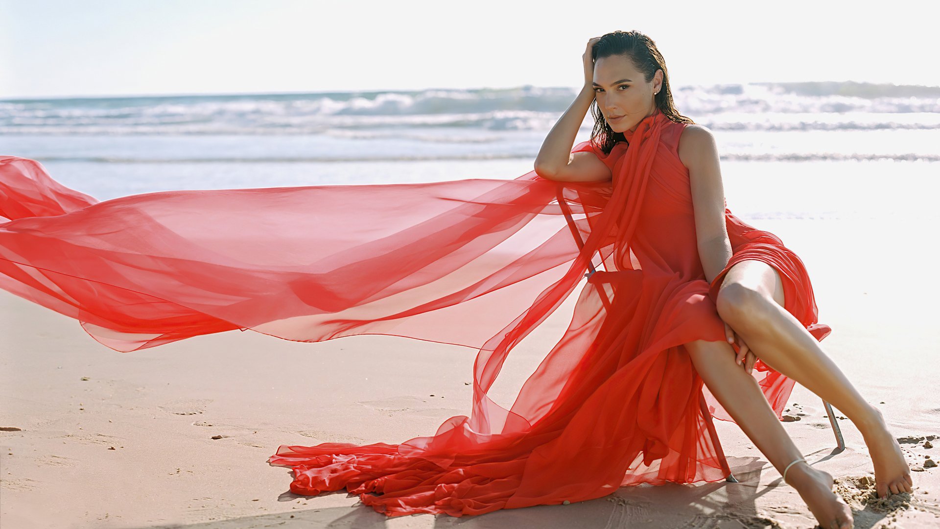 Israeli actress Gal Gadot poses on a beach wearing a flowing red dress in this 4K Ultra HD PC desktop wallpaper and background.