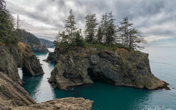 4K Ultra HD PC desktop wallpaper and background: rugged coastline with sea stacks topped by evergreens, a turquoise inlet and dramatic cloudy sky — nature, coastline