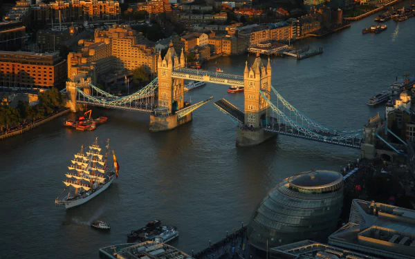 Aerial view of London’s Tower Bridge spanning the River Thames with boats sailing and city buildings illuminated at dusk.
