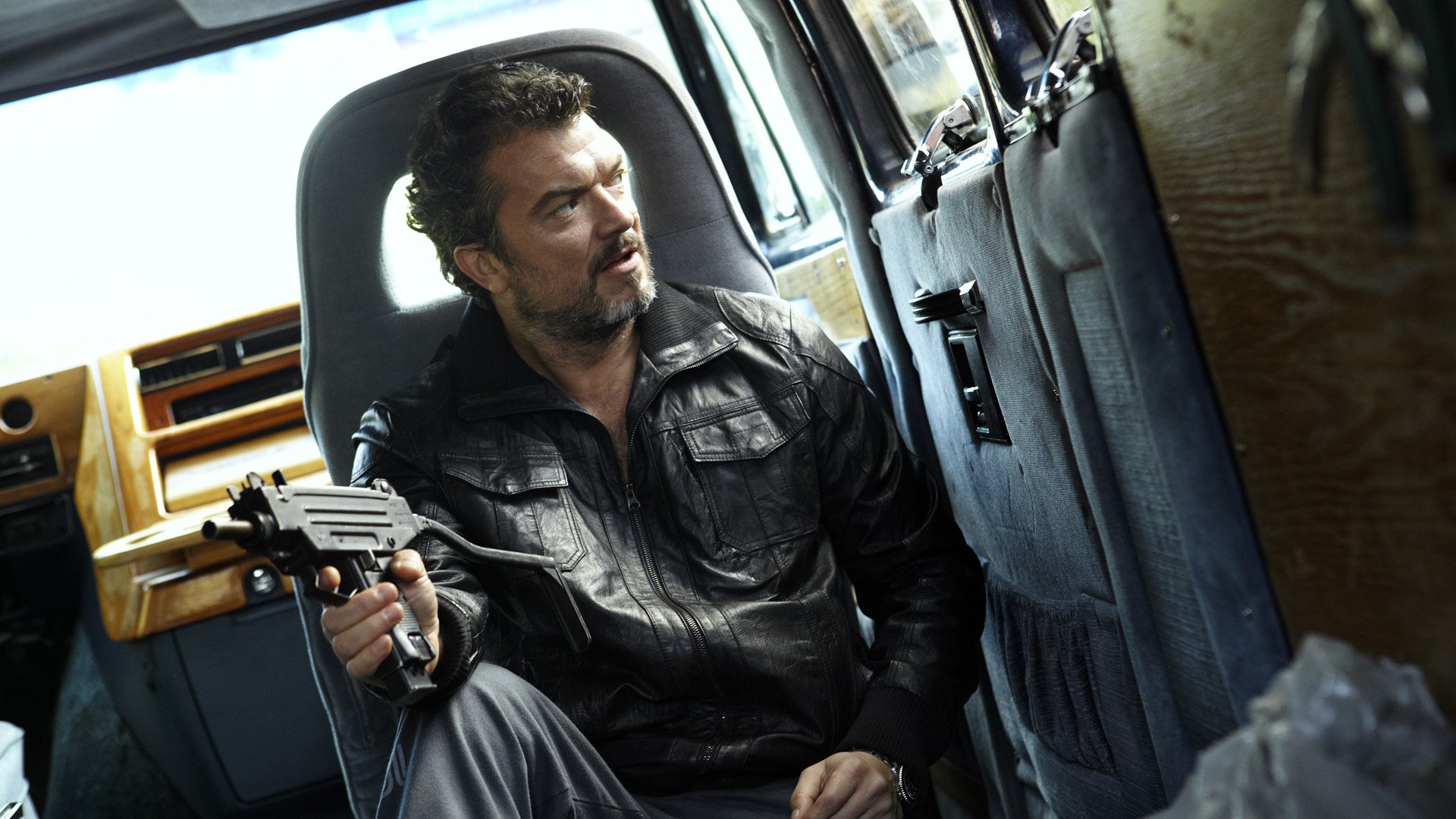 HD desktop wallpaper from Snabba Cash featuring a man holding a gun seated inside a vehicle with a tense expression.