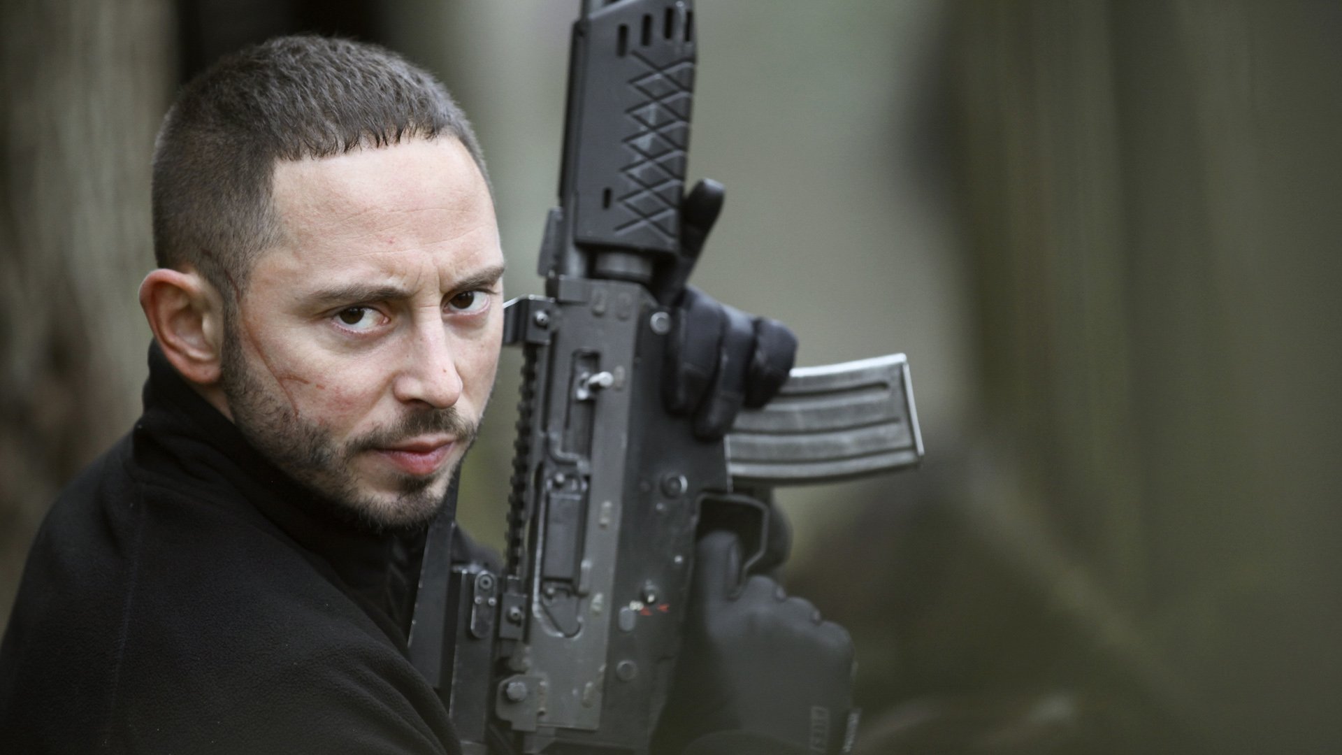 HD desktop wallpaper from Snabba Cash featuring a man with a rifle, focused and intense, set against a blurred background.