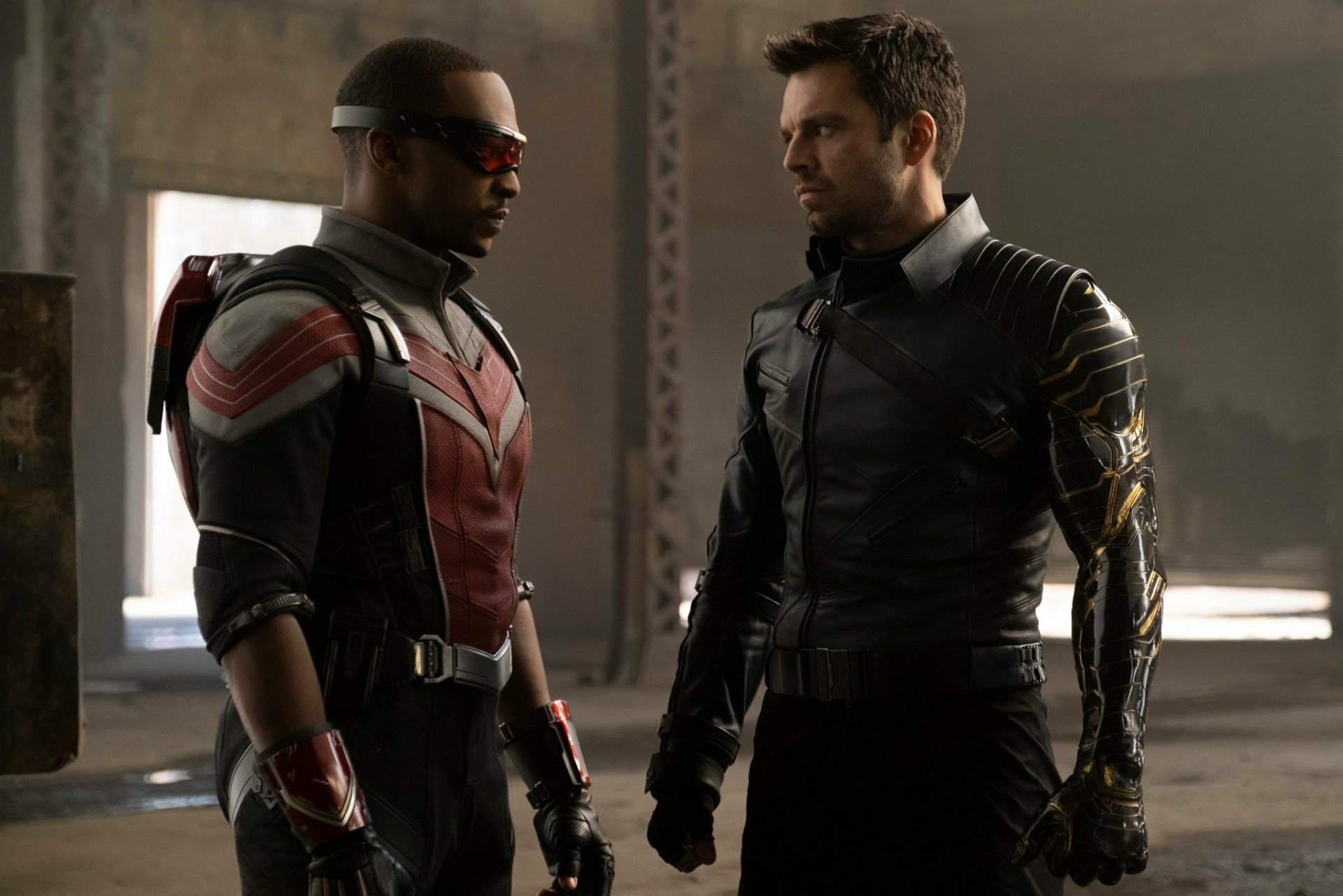 HD desktop wallpaper from the TV show The Falcon and the Winter Soldier: Sam Wilson (Falcon) and Bucky Barnes in tactical suits face off in a dim hangar.