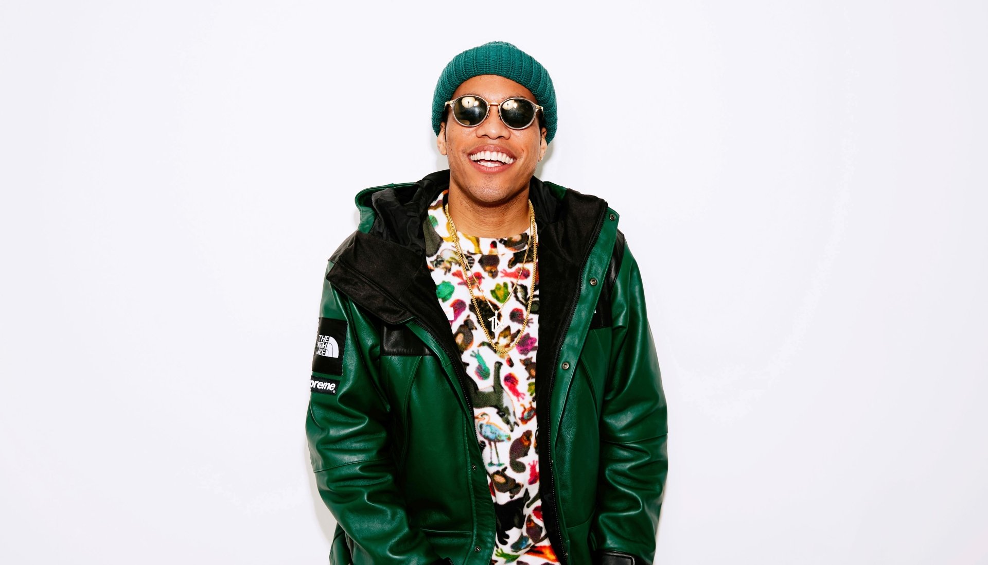 HD wallpaper of a smiling person in a green jacket and beanie, standing against a white background, tagged with Anderson .Paak.