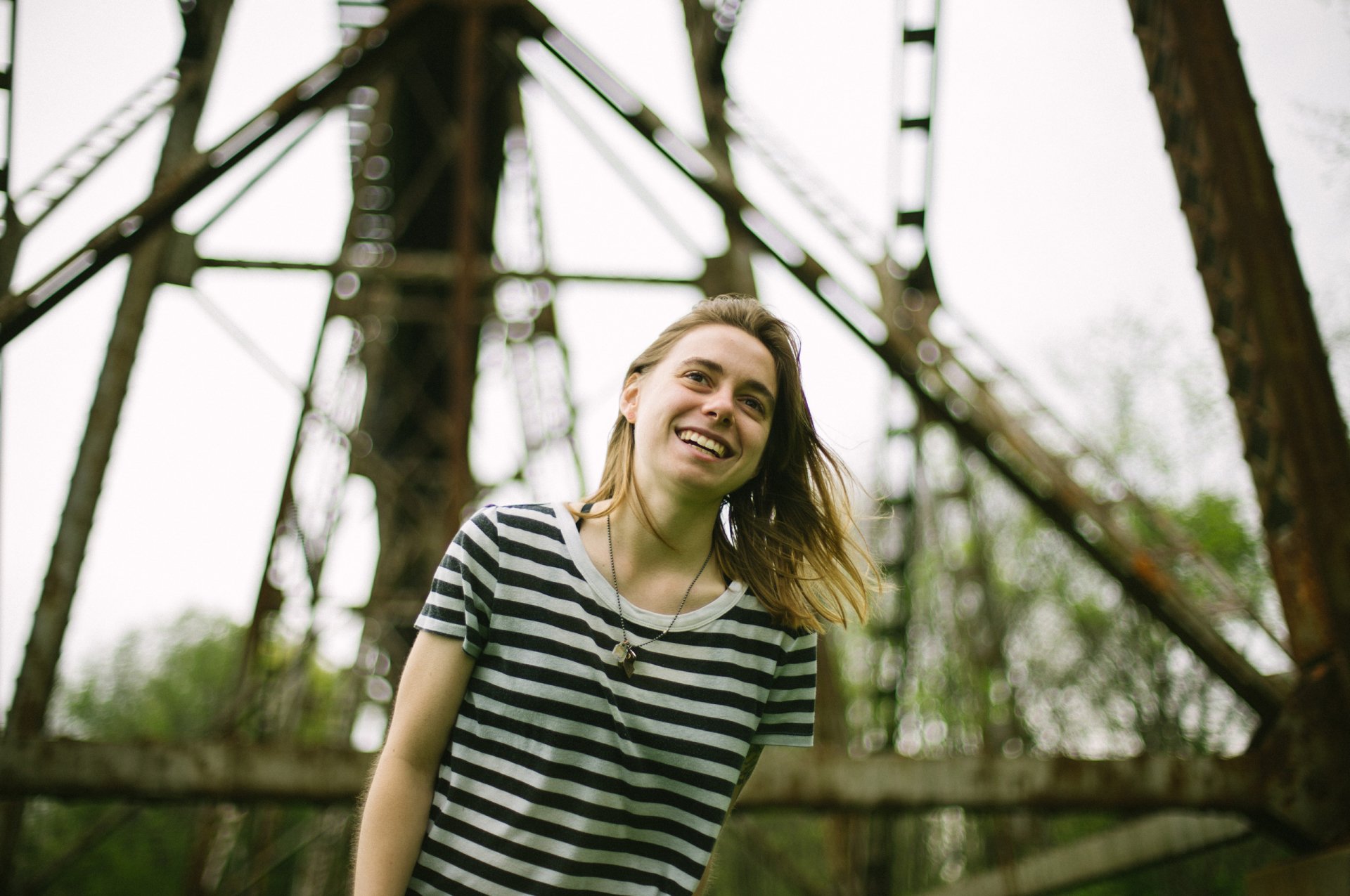 HD desktop wallpaper featuring a smiling person in a striped shirt standing in front of a bridge structure, associated with Julien Baker.