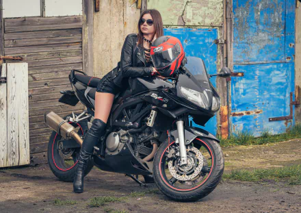Brunette woman wearing sunglasses, leather jacket, and boots poses on a Suzuki SV650S motorcycle against a rustic backdrop in this 4K Ultra HD Girls & Motorcycles wallpaper.