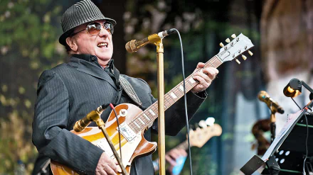 HD desktop wallpaper featuring a singer-songwriter performing on stage with a guitar in front of a microphone stand, providing a vibrant and inspiring musical background.