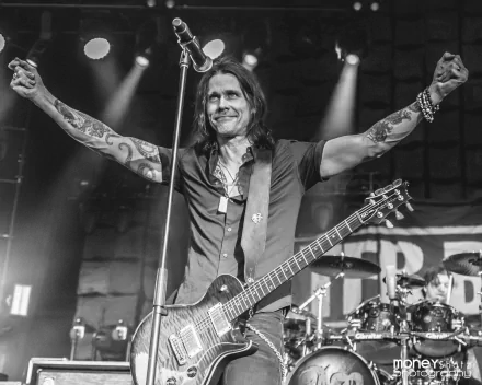 Black and white HD wallpaper of a male rock musician performing on stage with electric guitar and raised arms, set as a dynamic desktop background.