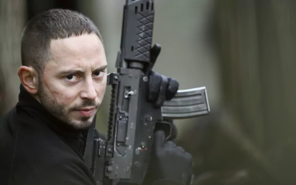 HD desktop wallpaper from Snabba Cash featuring a man with a rifle, focused and intense, set against a blurred background.