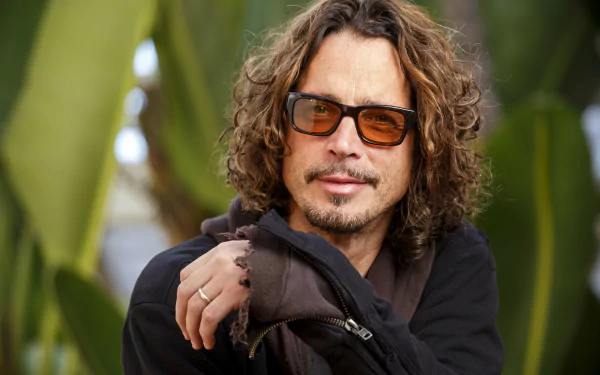 HD desktop wallpaper featuring a person with long curly hair and sunglasses, posing with arms crossed.